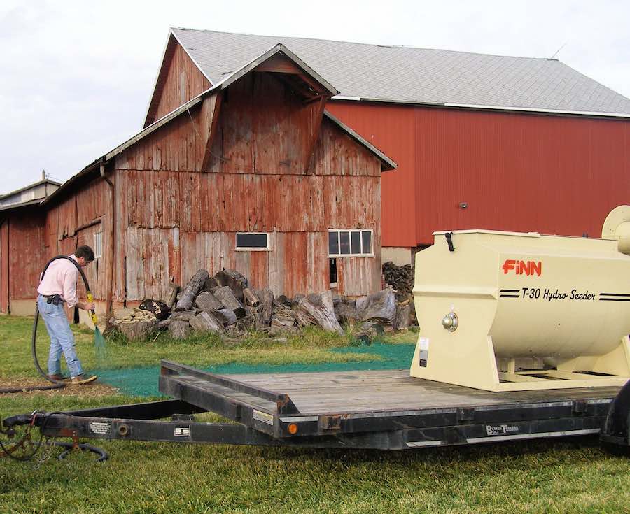 hydroseed vs sod vs grass seed which is better? A person hydroseeds a patch of lawn using a Finn hydroseeder.